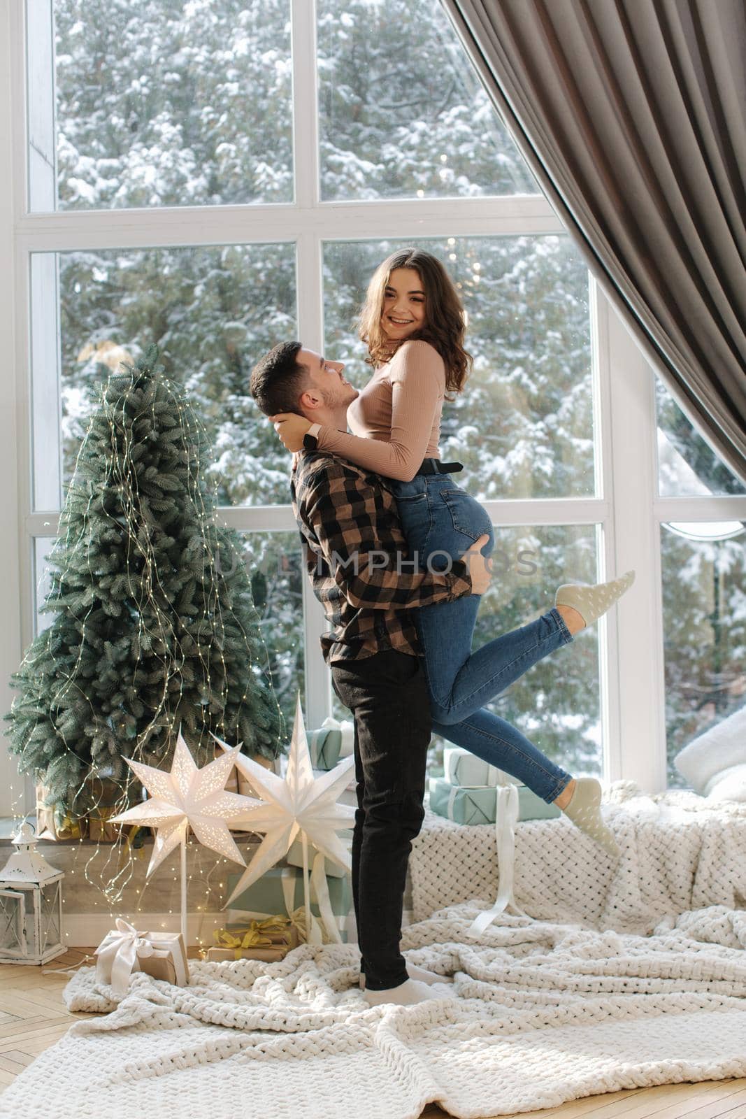 Handsome man with his girl friend enjoying of snowy weather outside and have fun near fir tree at home. by Gritsiv