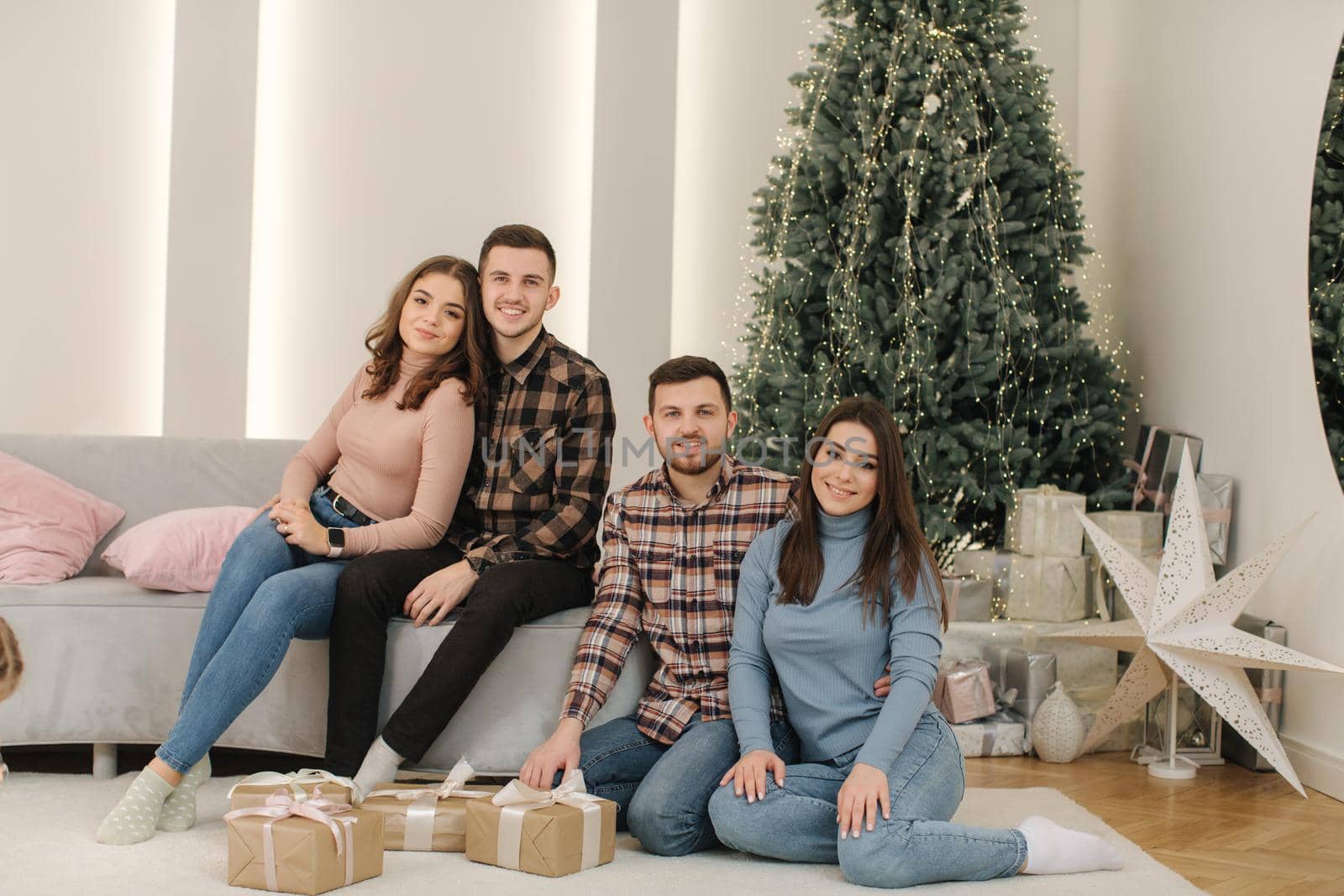 Two brother with their wifes at New Year photosession. Beautiful woman and man in front of fir tree. Christmas mood.