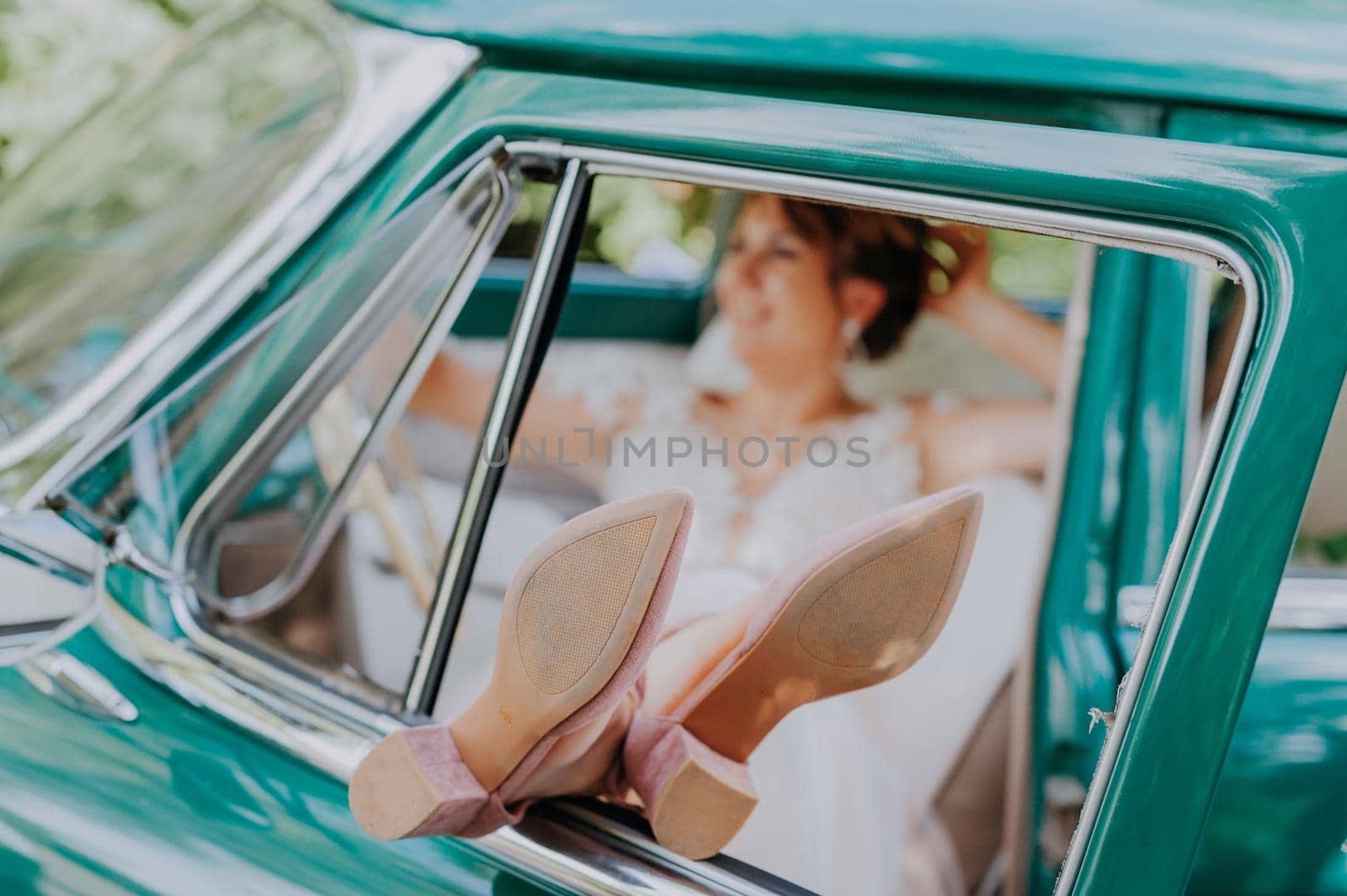 Wedding bride rest and have fun on green vintage retro car after wedding. Honeymoon concept. Car woman happy in old retro vintage car. Young woman driving on road trip on beautiful sunny summer day. by Andrii_Ko