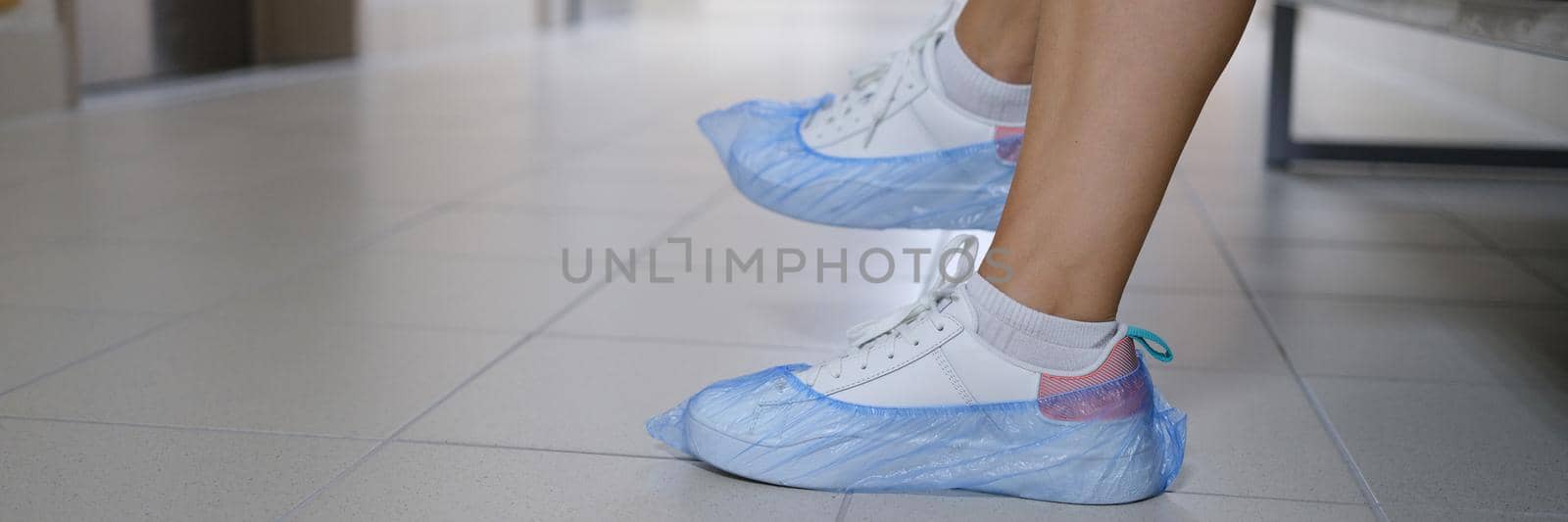 Women legs in sneakers with shoe covers in hospital corridor. Disposable shoe covers for visiting medical institutions concept