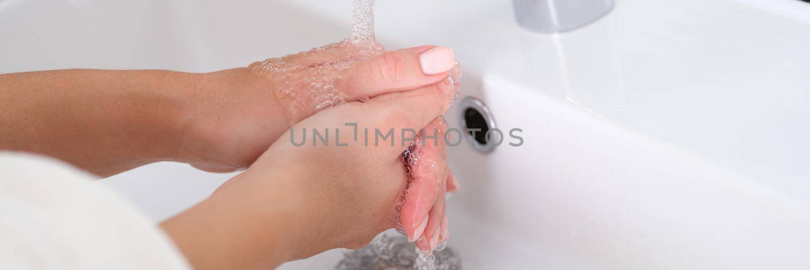 Woman washes hands under running water in sink. Hand hygiene concept