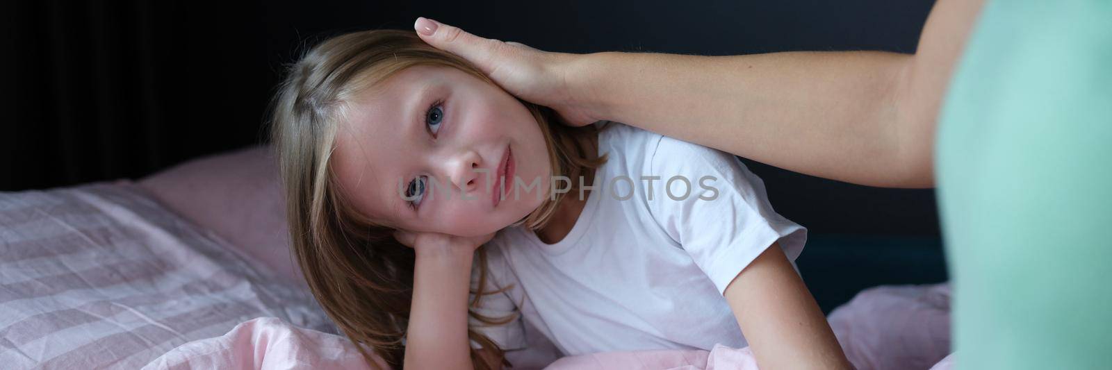 Mom strokes head of little girl sitting in bed closeup by kuprevich