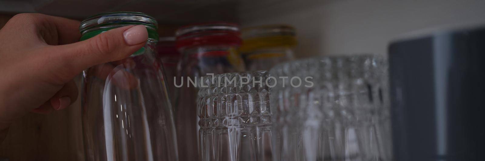 Woman hand pulls out glass cup from cabinet in kitchen by kuprevich