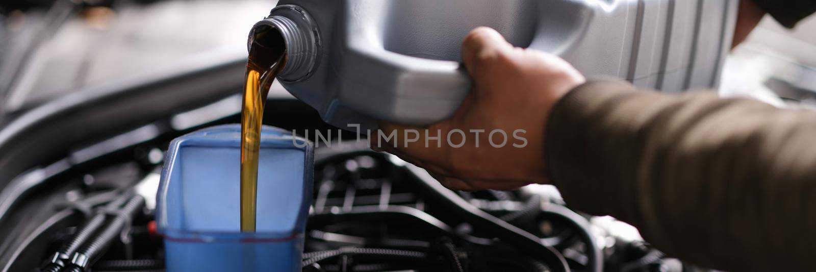 Locksmith mechanic pours engine oil into plastic container on motor engine. Oil change in car engine concept