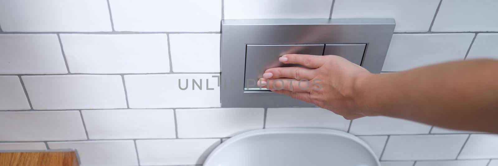 Female hand presses flush button in toilet. Flush cistern button concept