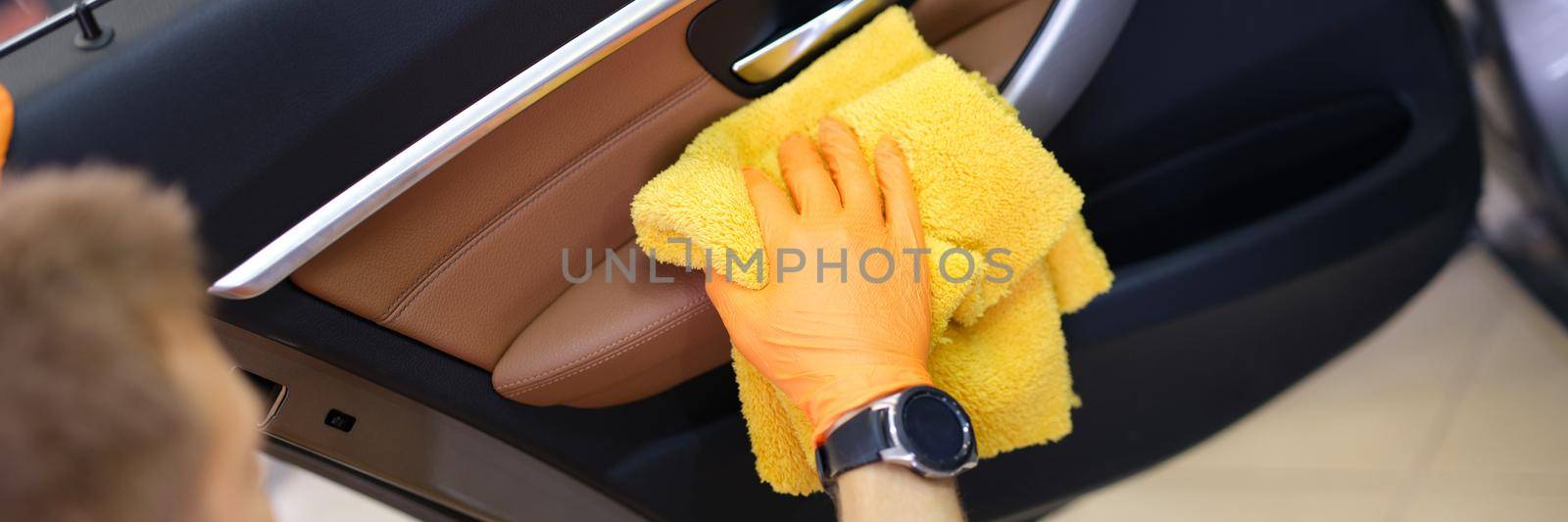 Male washer in gloves wipes car door with microfiber. Car wash services concept