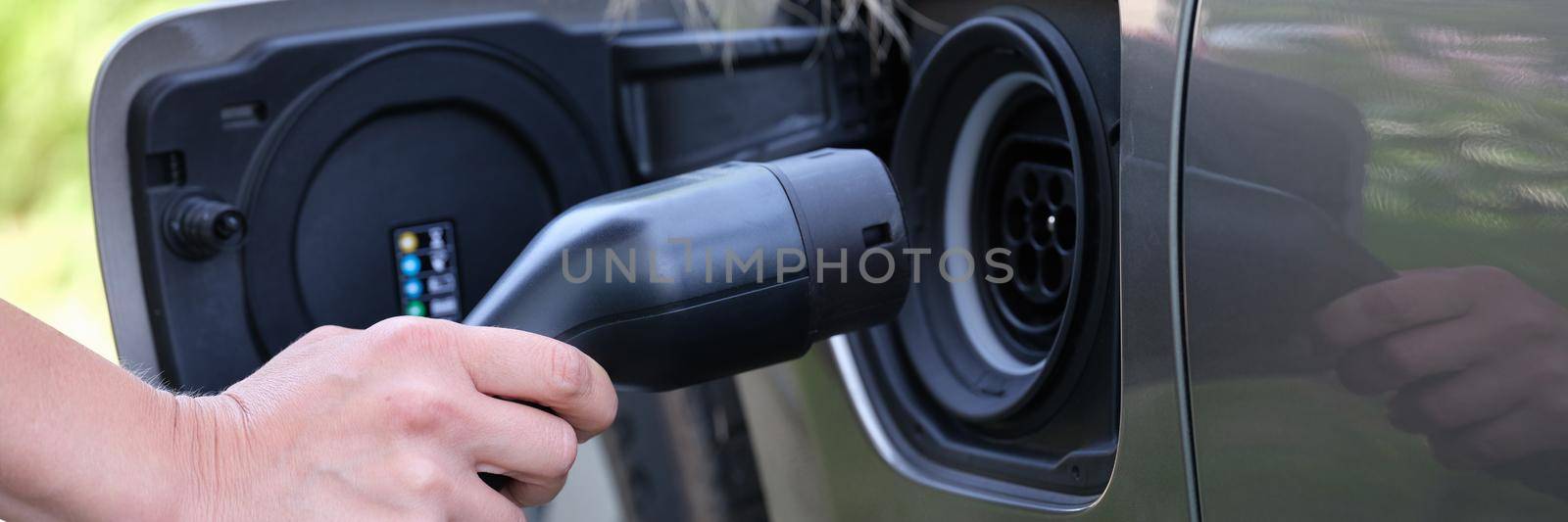 Female hand inserts plug for charging electric car. Fueling hybrid cars concept