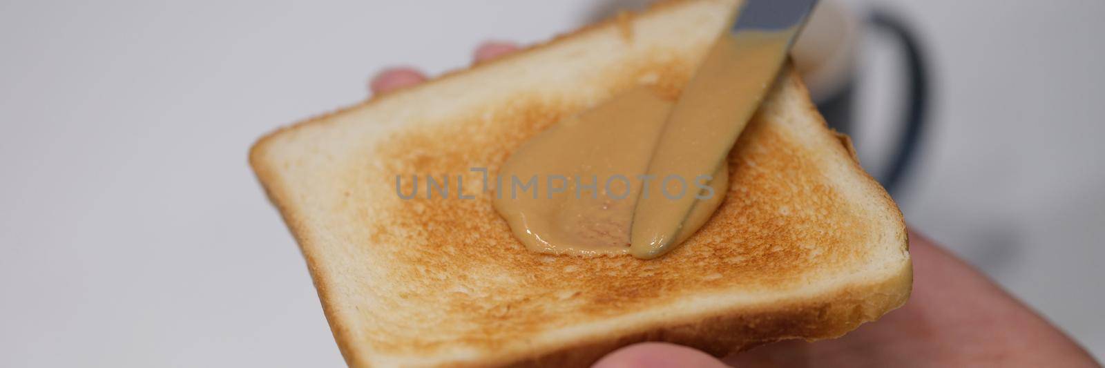 Woman spreads peanut butter on toast with knife. Benefits and harms of peanut butter sandwiches in the morning concept