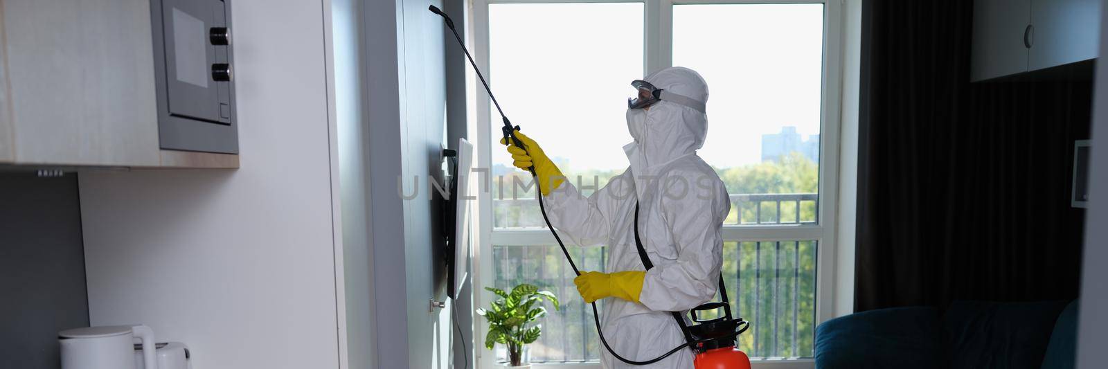 Person in white protective suit, mask and gloves with balloon disinfection in kitchen. Treatment of living quarters from insects and cockroaches concept