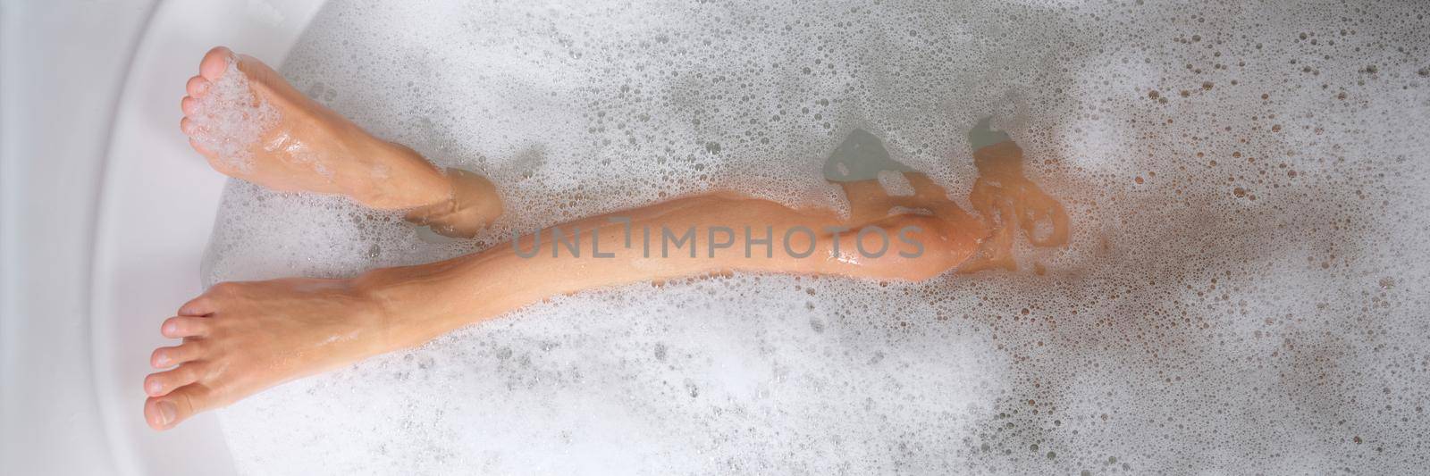 Women beautiful slender legs in bath with water and foam by kuprevich