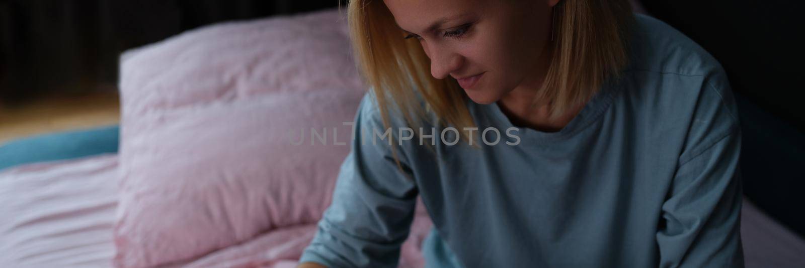 Woman sits on bed and looks into smartphone. Using mobile phone before bedtime concept