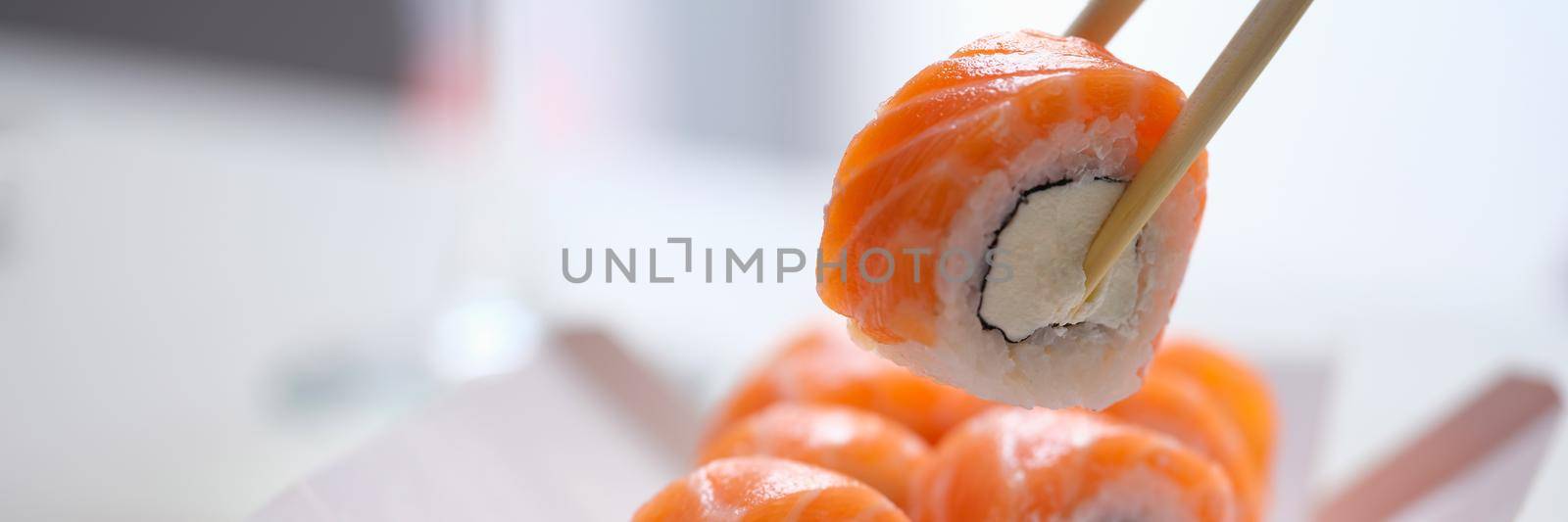 Hand with disposable chopsticks holds sake nigiri sushi with salmon fish. Cooking sushi at home concept