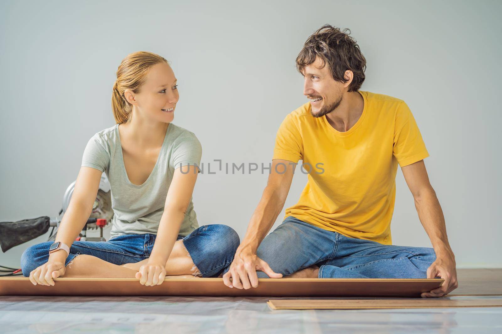 Married couple installing new wooden laminate flooring on a warm film floor. Infrared floor heating system under laminate floor.