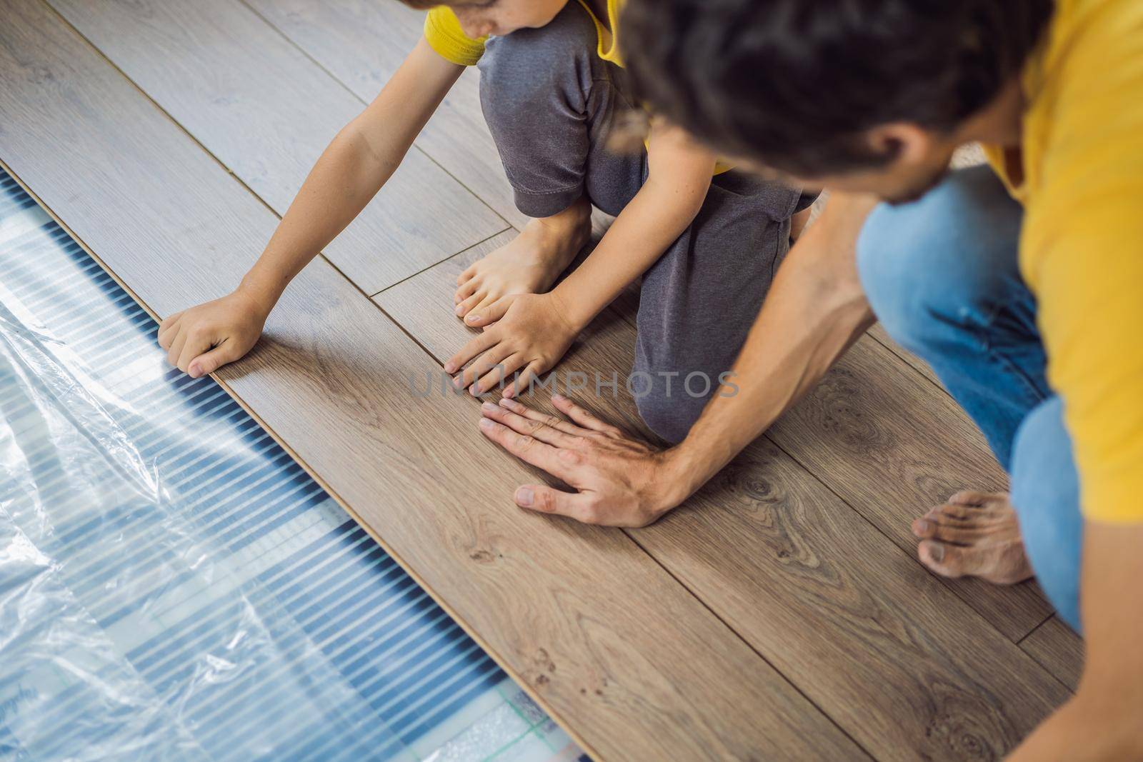 Father and son installing new wooden laminate flooring on a warm film floor. Infrared floor heating system under laminate floor by galitskaya