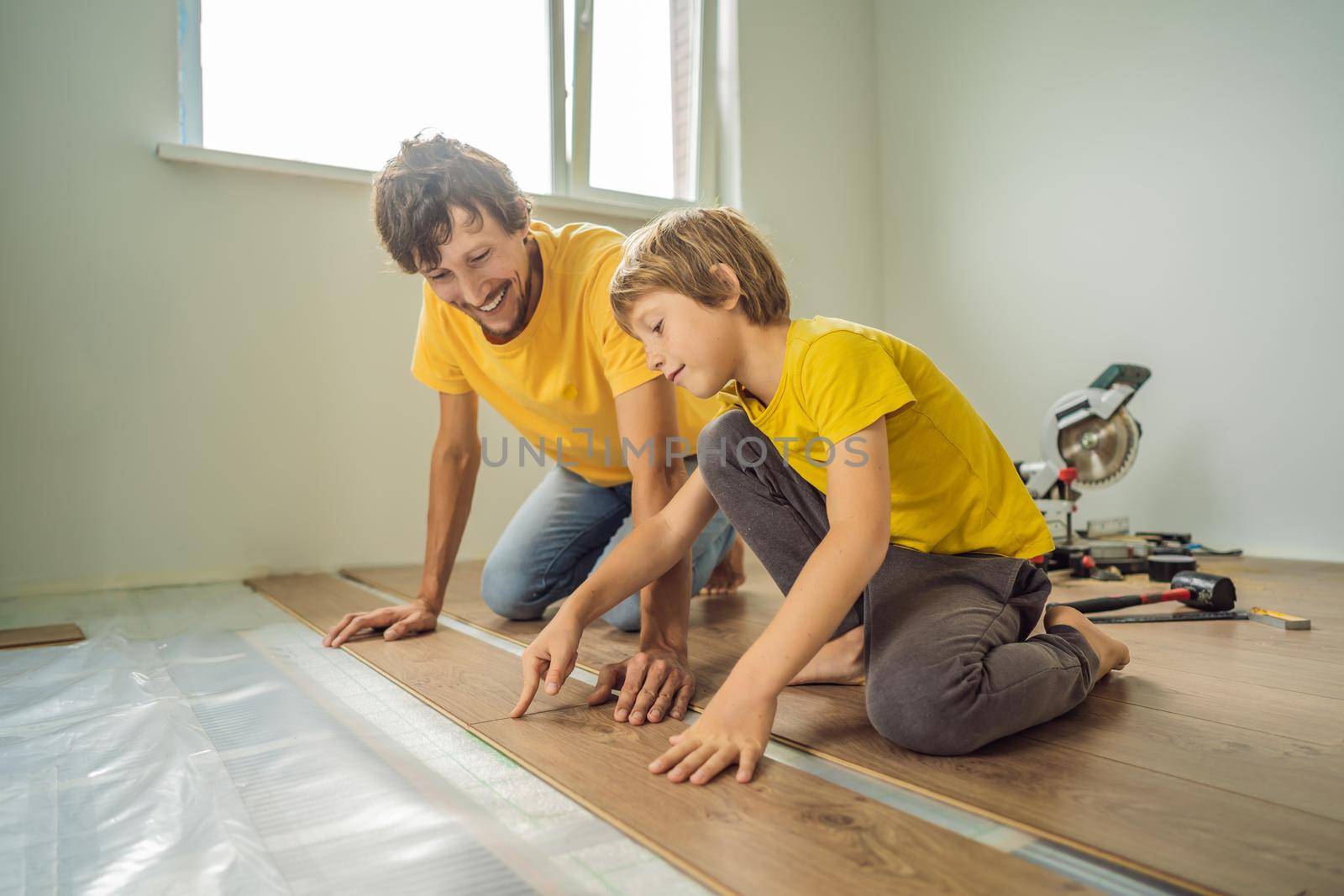 Father and son installing new wooden laminate flooring on a warm film floor. Infrared floor heating system under laminate floor.