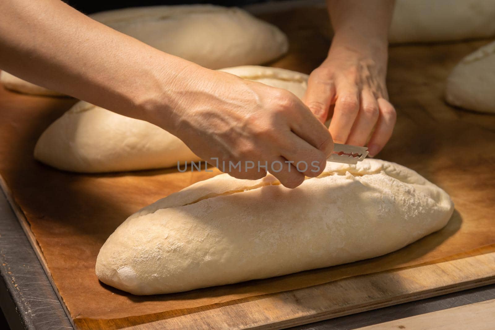 Close-up of a baker's female hands cutting a loaf of dough into a loaf of bread with a blade before baking in the oven. Craft craft bread production.