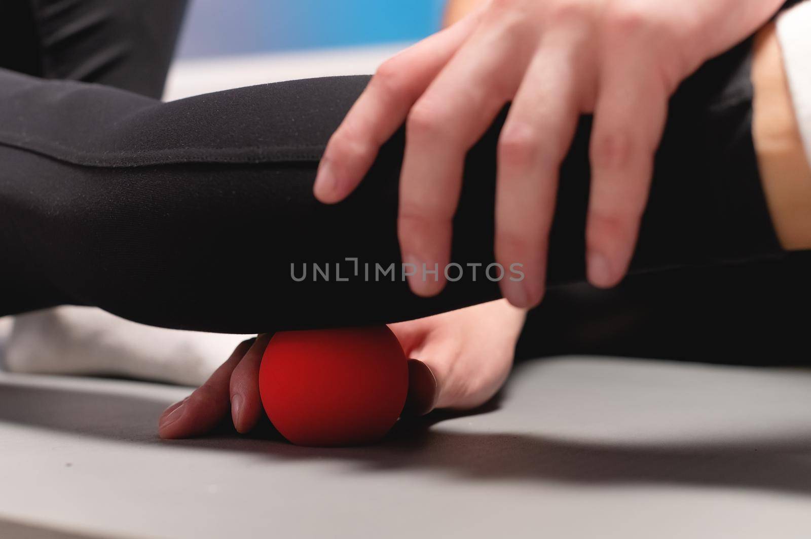 Young caucasian male masseur helping a female client to do myofascial massage of the calf muscle with a red massage ball. Close-up.