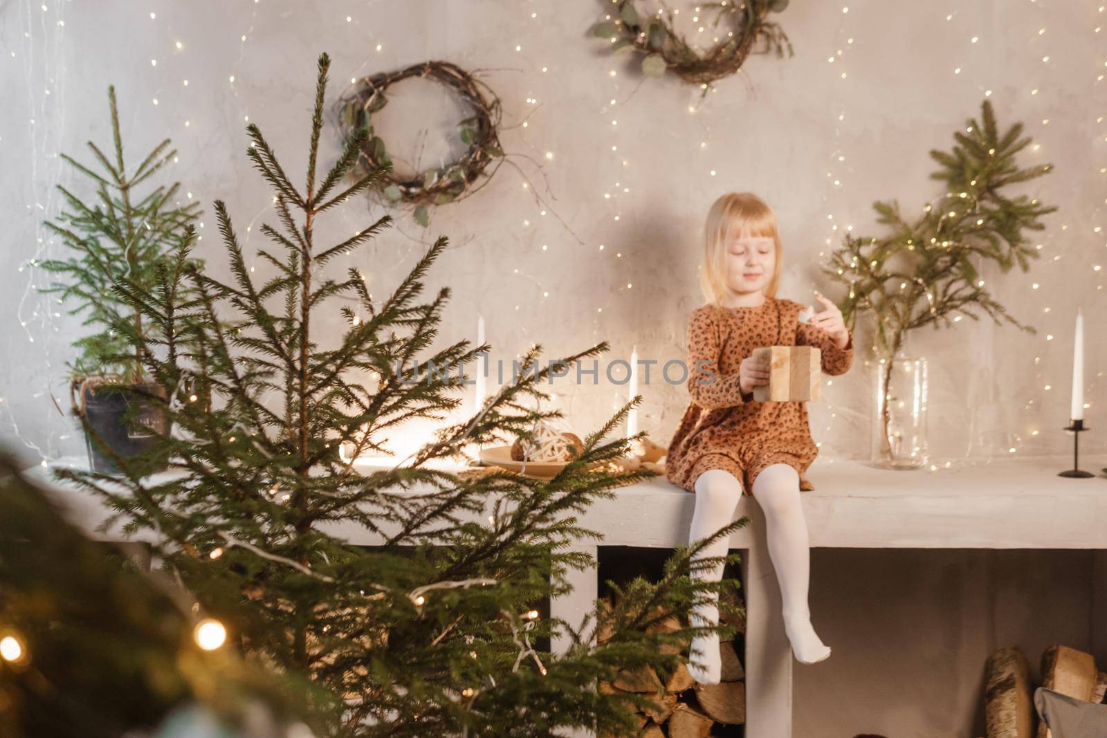 A girl is playing on Christmas Eve in a beautiful house decorated for the New Year holidays. Scandinavian-style interior with live fir trees and a wooden staircase.