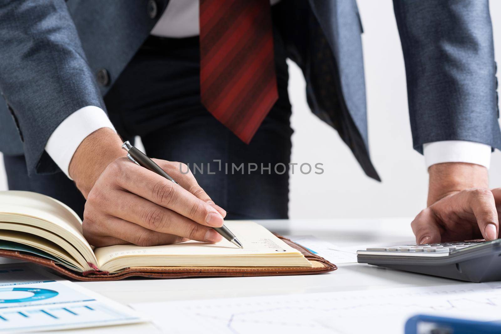Close-up businessman hand writing to do list in diary at desk. Financial expertise and consulting. Manager in suit and tie planning day with personal organizer. Time management and work organization.