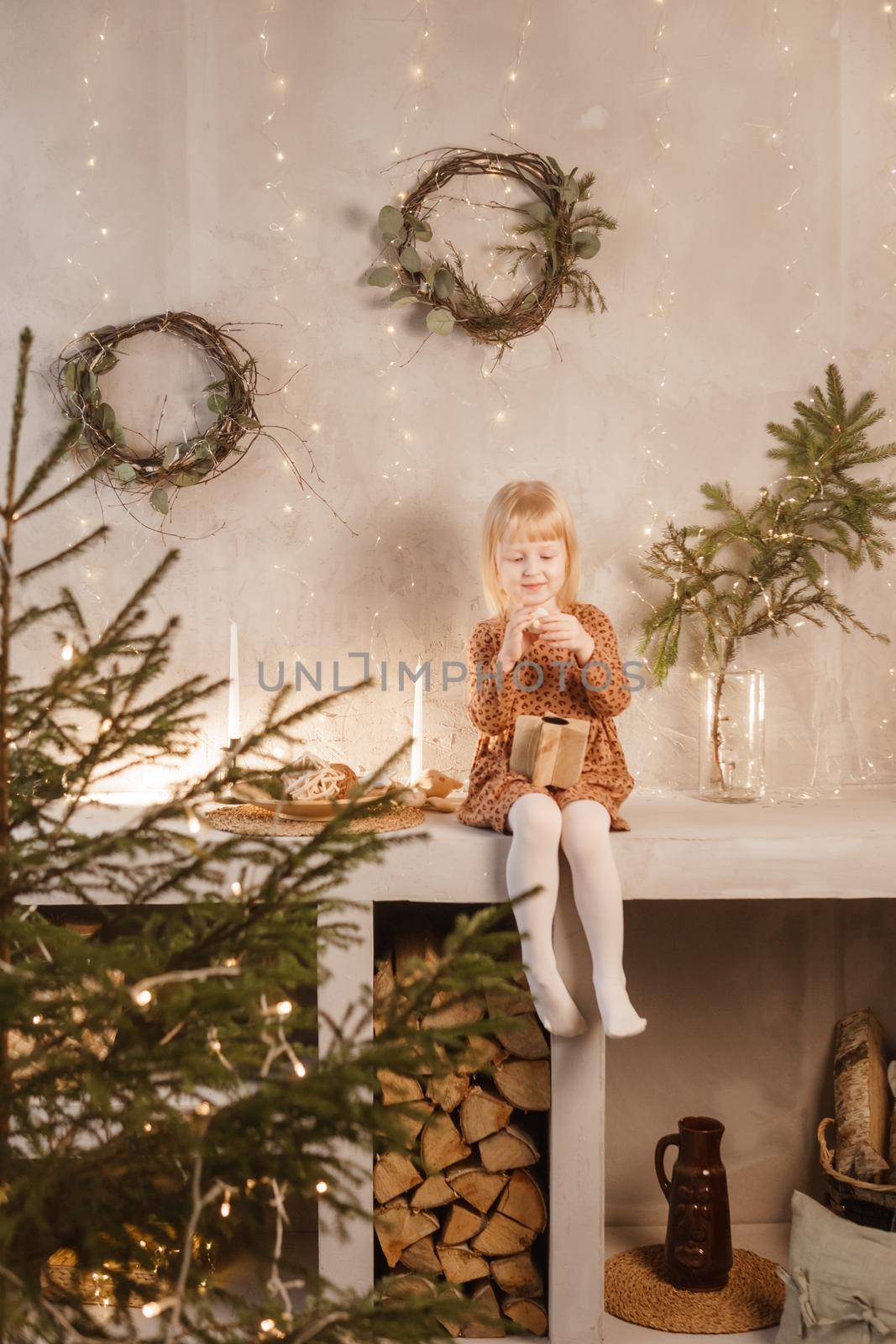 A girl is playing on Christmas Eve in a beautiful house decorated for the New Year holidays. Scandinavian-style interior with live fir trees and a wooden staircase.