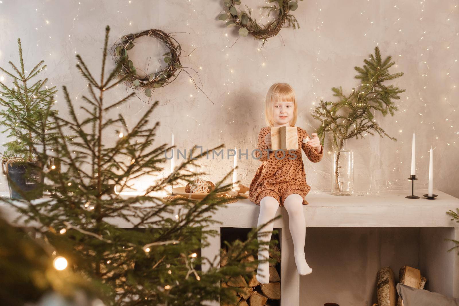 A girl is playing on Christmas Eve in a beautiful house decorated for the New Year holidays. Scandinavian-style interior with live fir trees and a wooden staircase.
