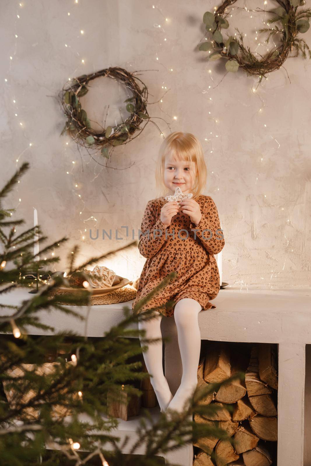 A girl is playing on Christmas Eve in a beautiful house decorated for the New Year holidays. Scandinavian-style interior with live fir trees and a wooden staircase.