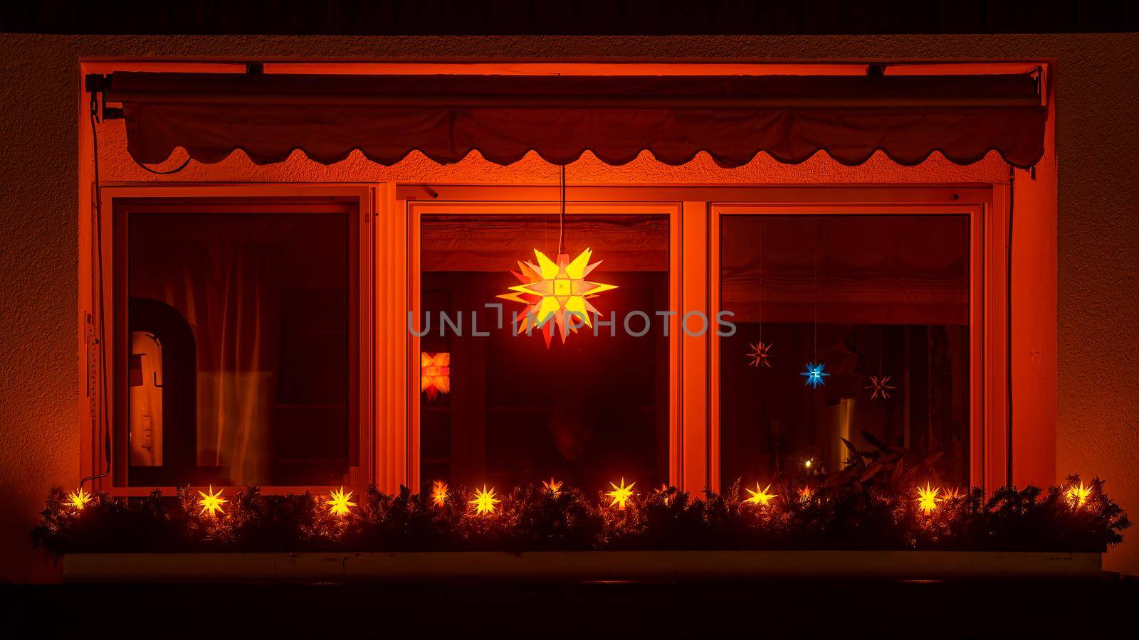 Bright shining X-Mas star in a window of a night. Traditional decor of the Christmas season with the view over an illuminated balcony. by AllesSuper