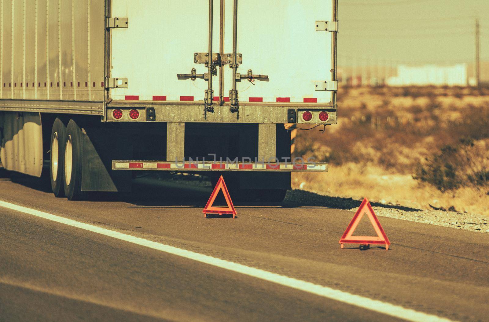 Heavy Transportation Theme. Broken Semi Truck on Side of a Highway Trailer Close Up and Warning Triangles. Roadside Asssitance.