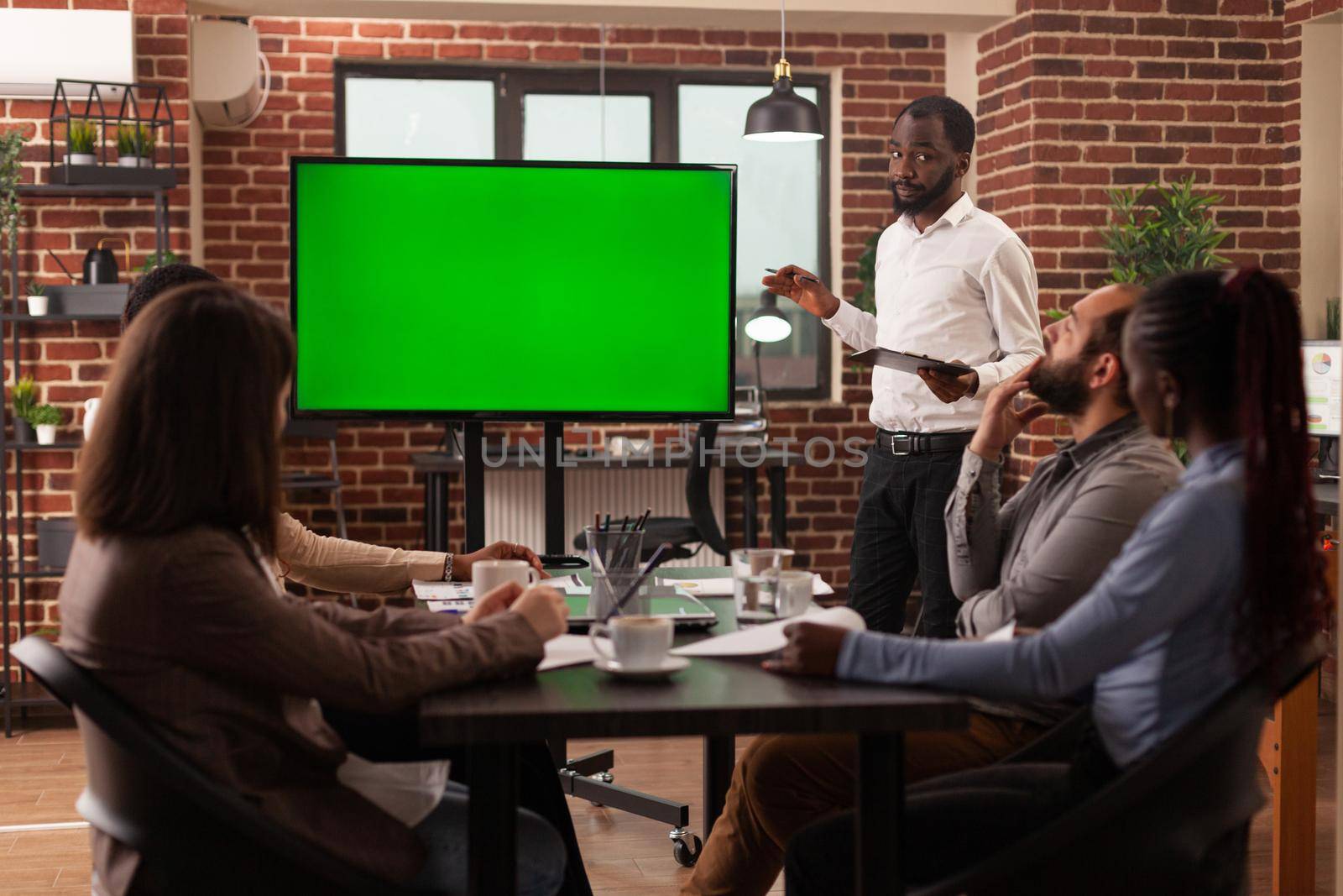 Businessman explaining management strategy using mock up green screen chroma key monitor with isolated display working in startup company office. Businesspeople brainstorming ideas