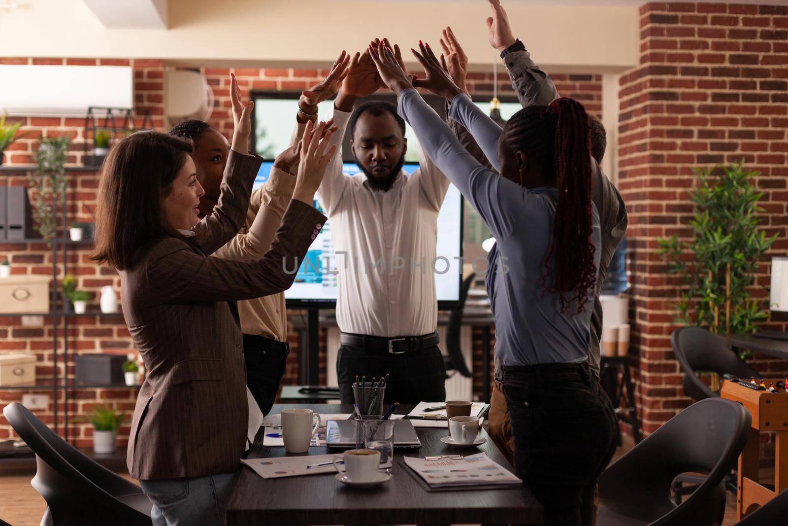 Successful excited diverse businesspeople celebrating winning business partnership rising hands while working in startup company office. Happy businessteam enjoying triumph at workplace