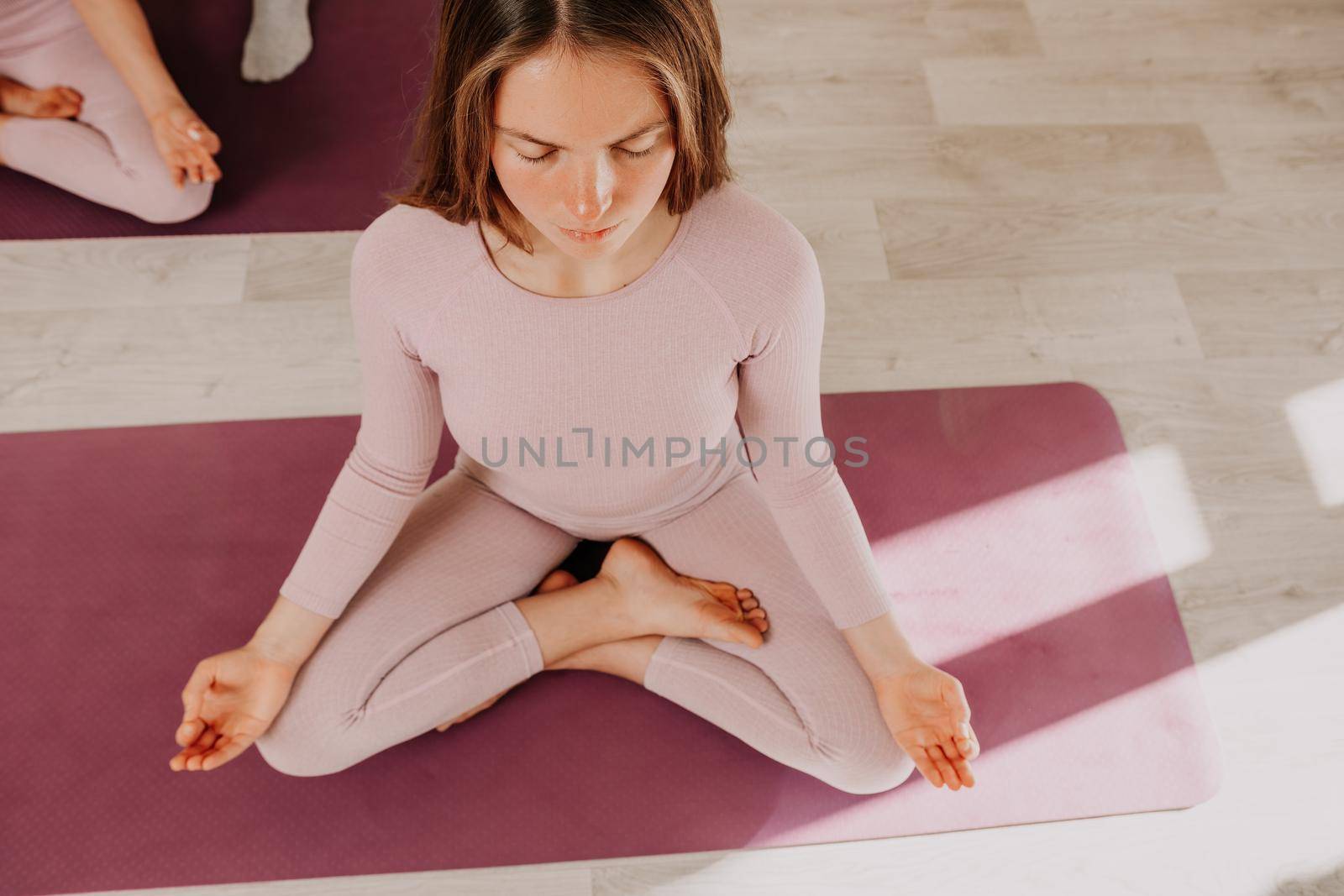 Young woman with long hair in white swimsuit and boho style braclets practicing outdoors on yoga mat by the sea on a sunset. Women's yoga fitness routine. Healthy lifestyle, harmony and meditation