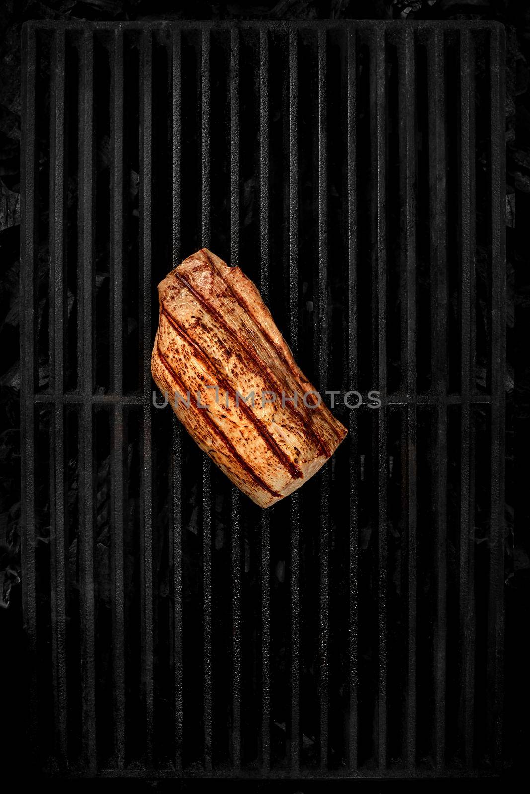 Top view of grilled veal tenderloin lying on black cast iron grill grate over cold coals. BBQ cooking concept. Vertical image