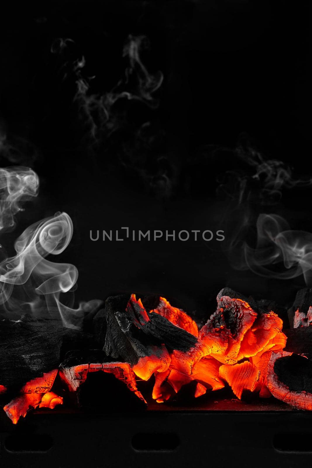 Red hot smouldering charcoals on metal tray of bbq grill on black background with light white smoke. Vertical image