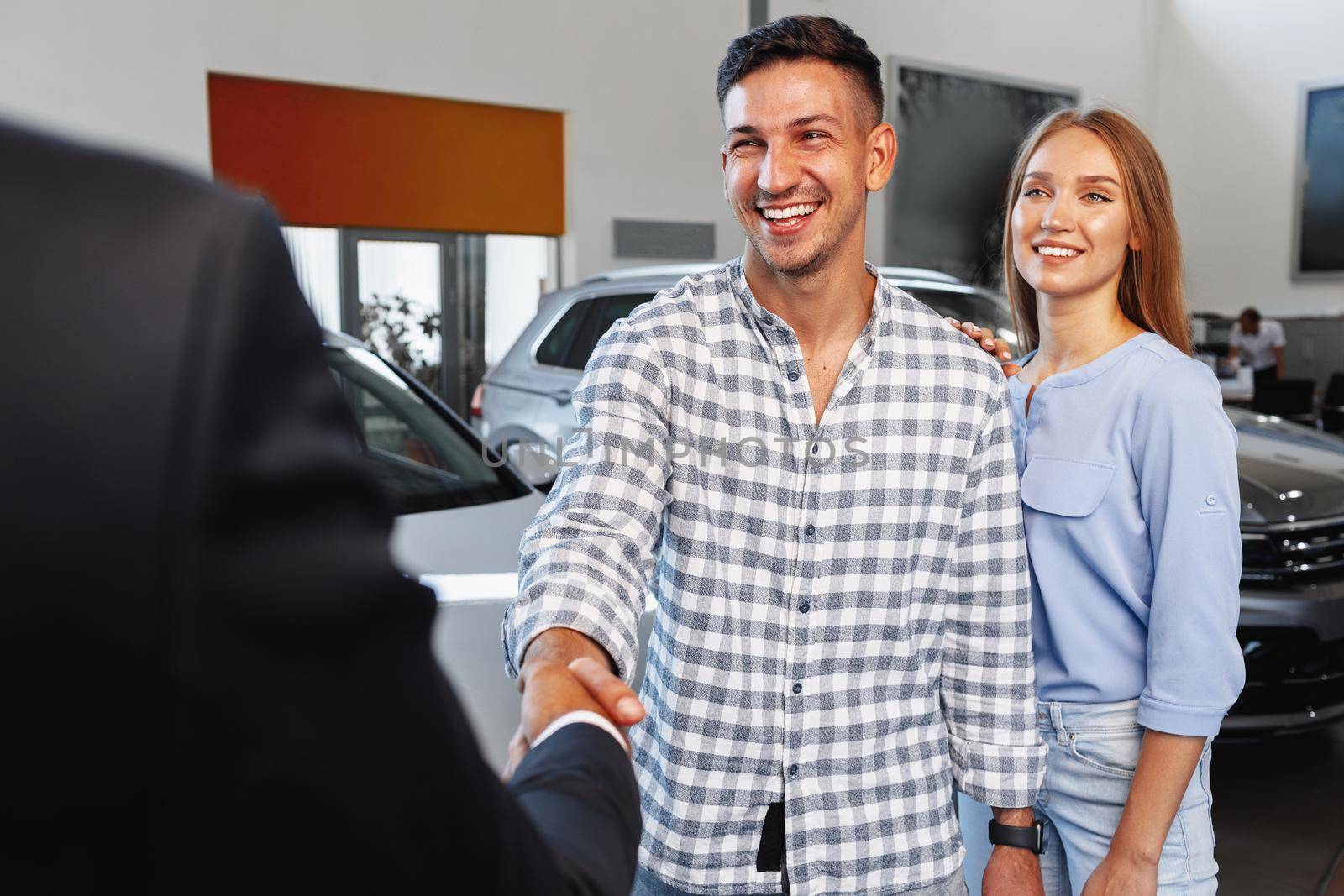 Cherrful young couple at the dealership buying a new car indoors