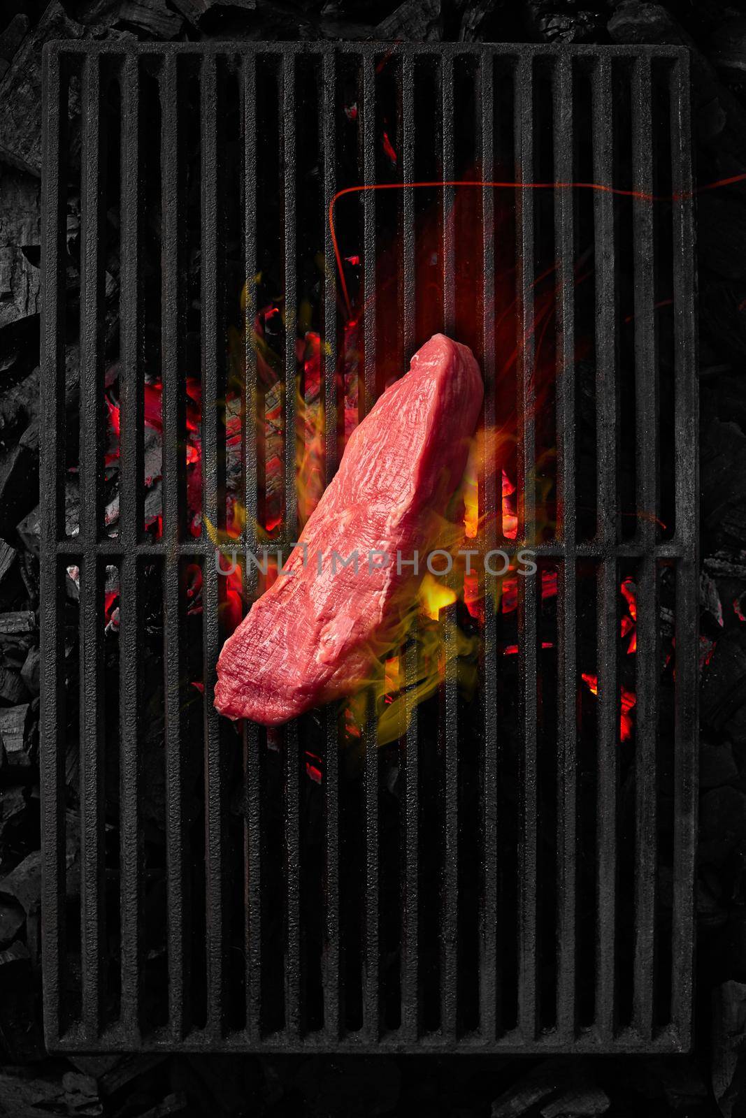 Piece of veal tenderloin cooking on black grill grate over burning charcoals by nazarovsergey