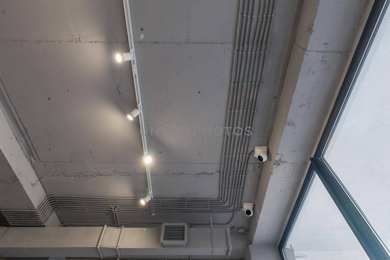 Abstract loft interior of concrete grey ceiling with air ventilation and security camera. Interior architecture and ceiling design of industrial loft building decorated with modern lamps by panophotograph