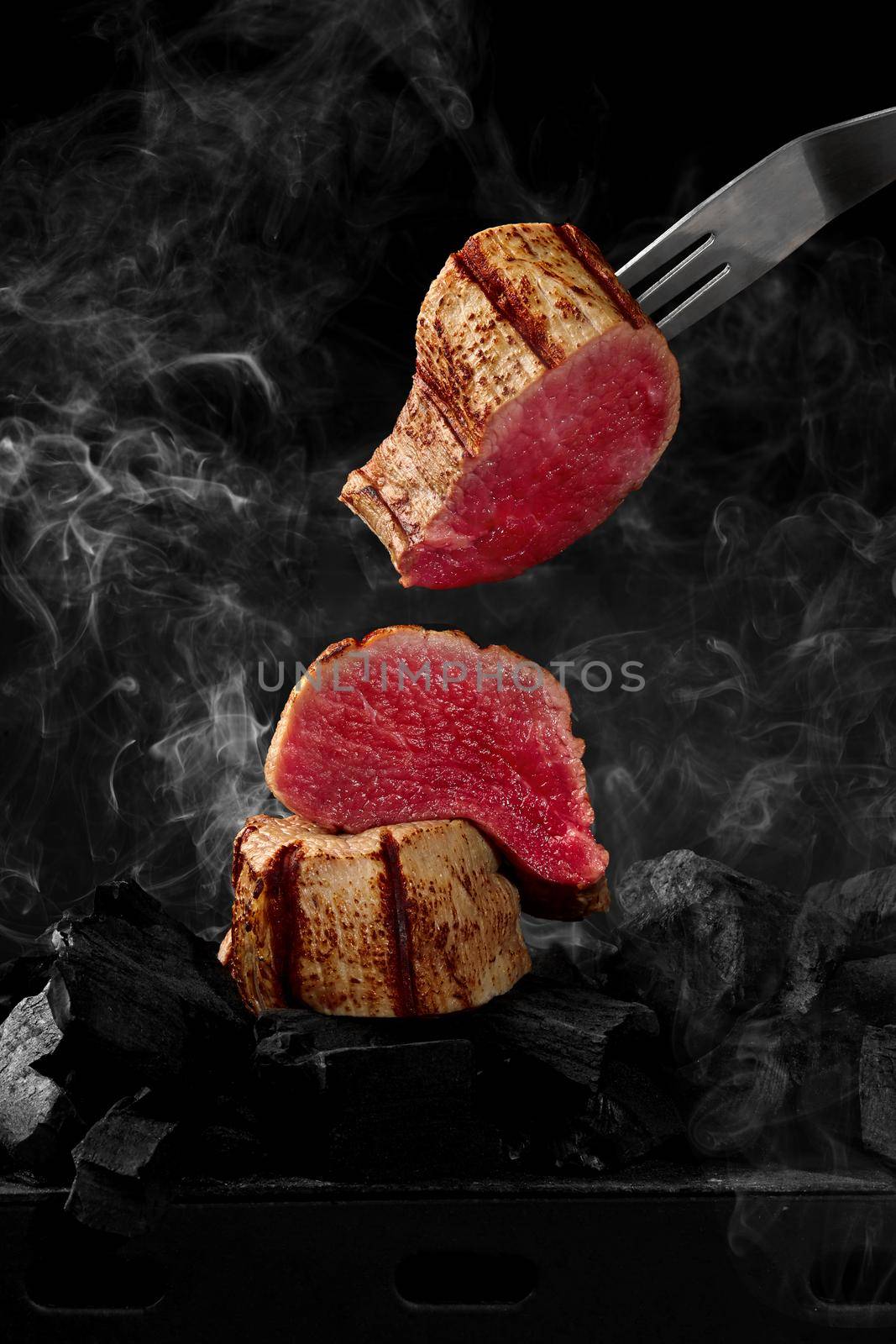 Pieces of beef tenderloin cooking on grill over smoking embers by nazarovsergey