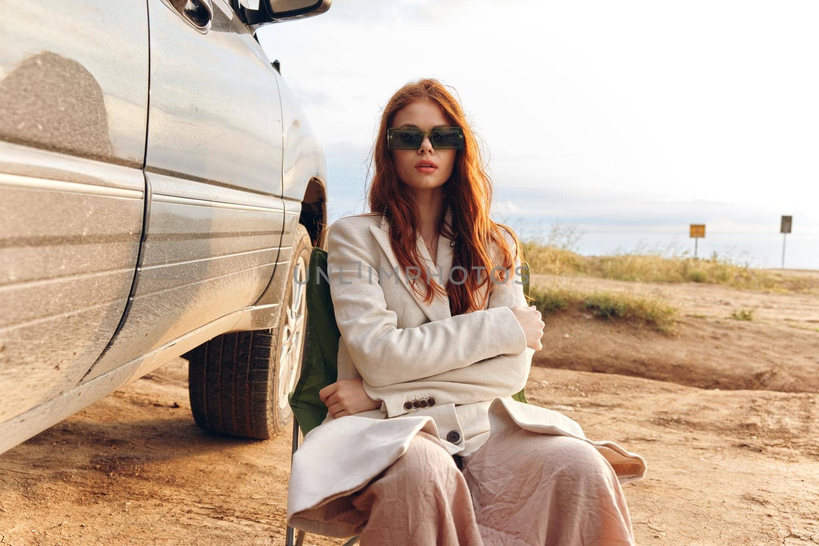 pretty woman in a coat outdoors sitting on a chair near the car endless field. High quality photo