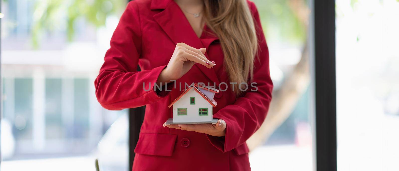 Hands woman protect wooden house model. Home insurance concept.