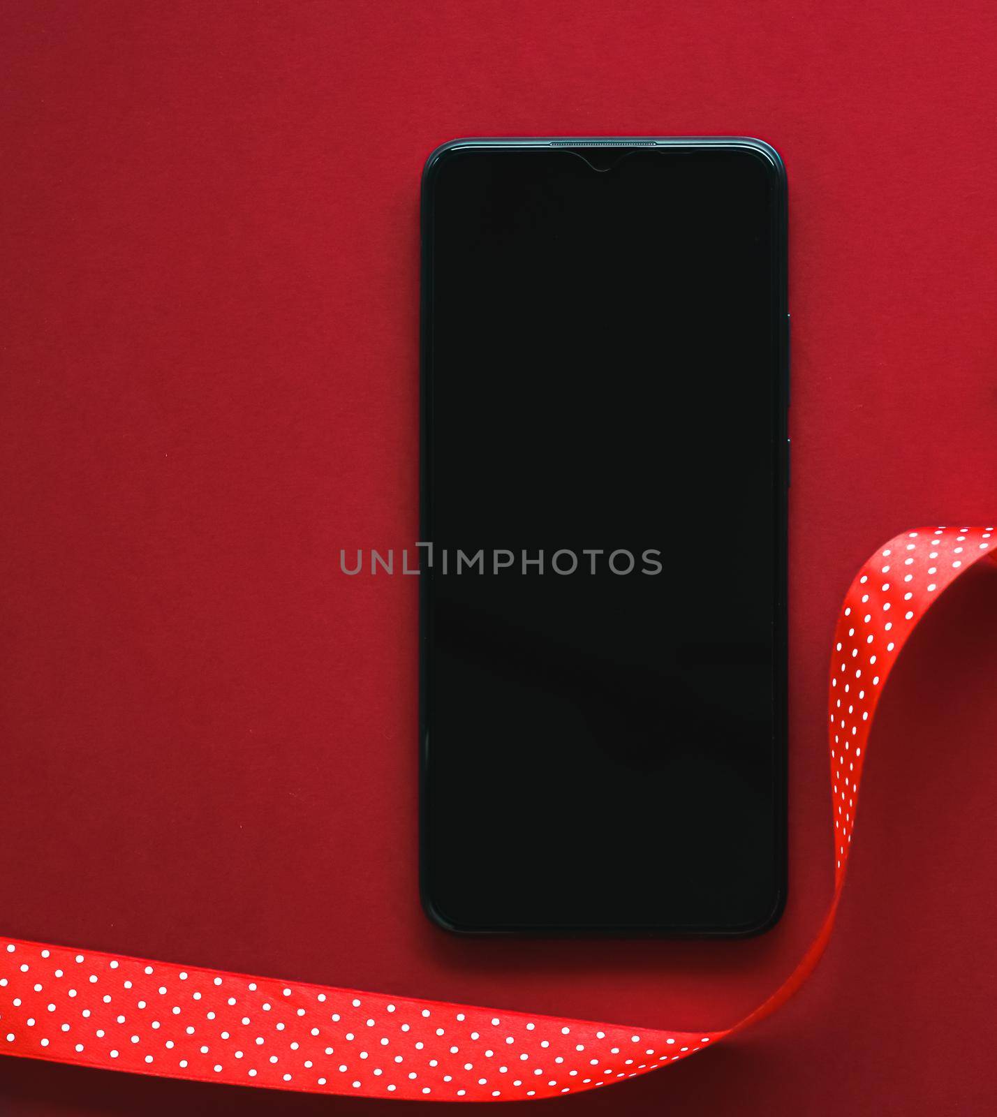 Christmas phone app and holiday message concept. Smartphone with blank black screen and xmas decoration on red background as flat lay mockup design.