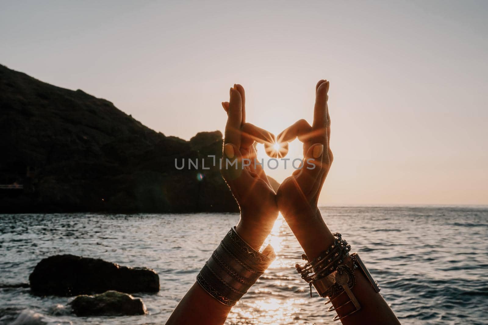 Middle aged well looking woman in white swimsuit and boho style braclets practicing outdoors on yoga mat by the sea on a sunset. Women's yoga fitness routine. Healthy lifestyle, harmony and meditation by panophotograph