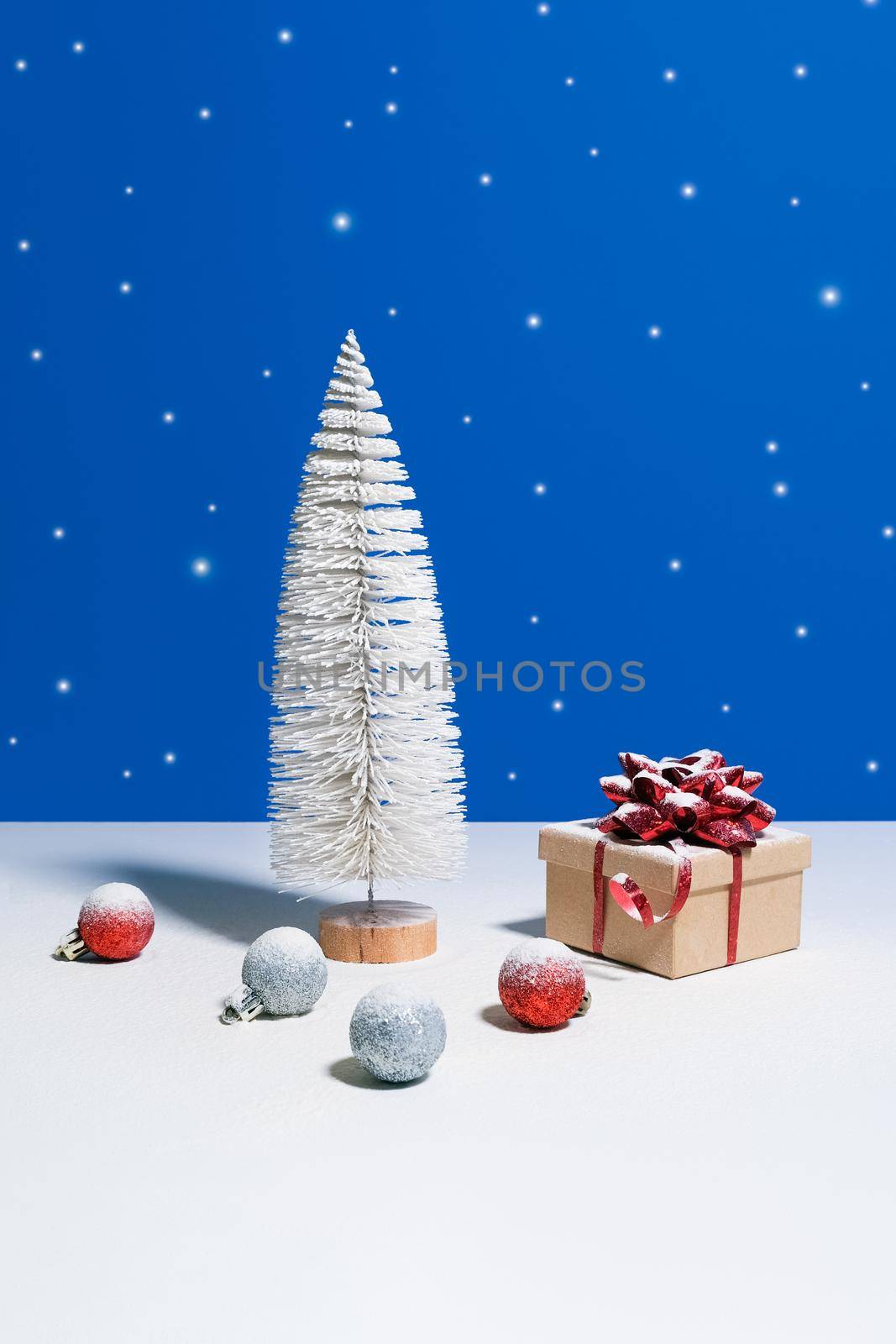 Beautiful Christmas or New Year banner. Toy Christmas tree, gift box with red bow and Christmas baubles on blue background with snow falling on the background
