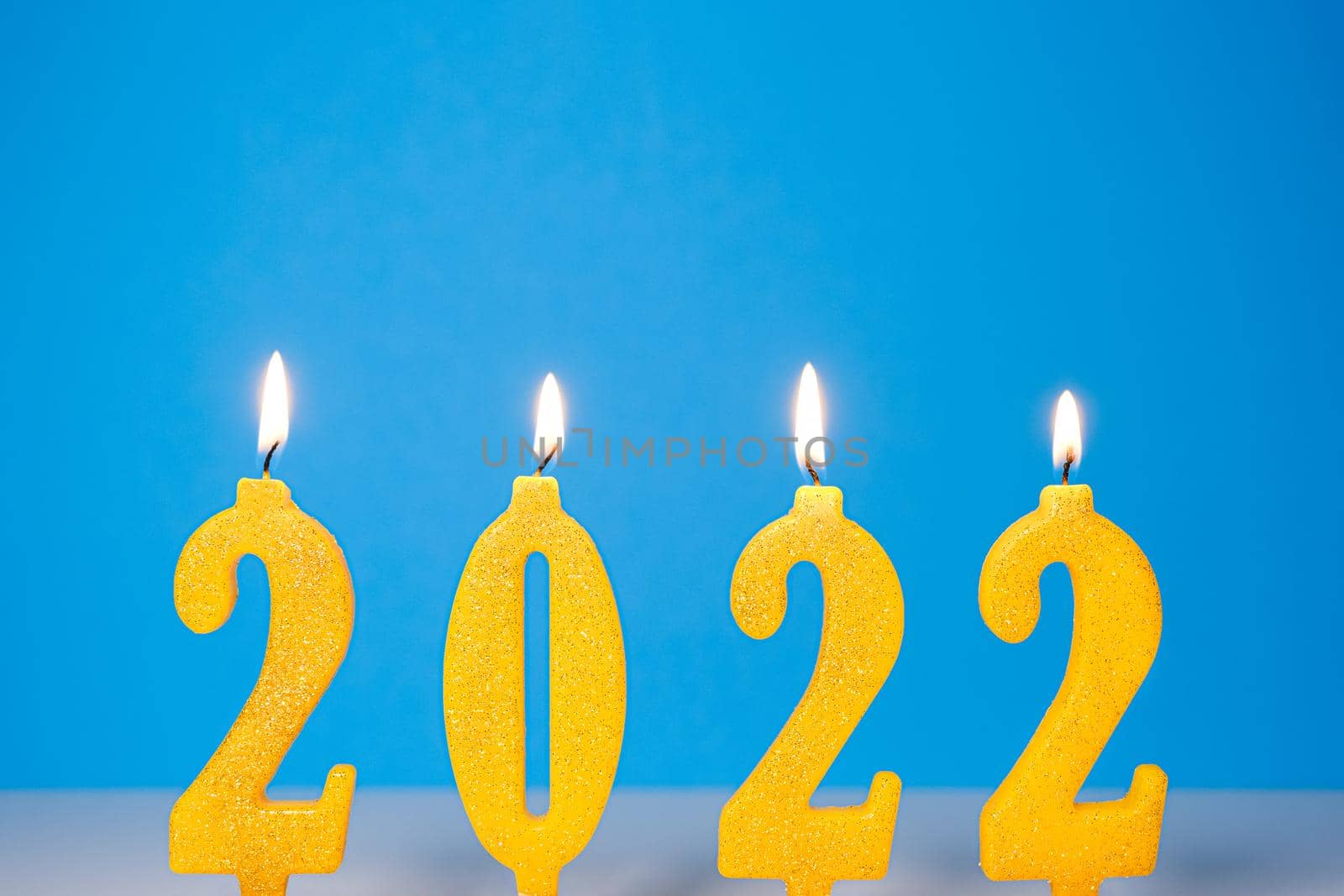 Holiday background of burning yellow candles 2022 Happy New Year concept Burning yellow and golden 2022 candles isolated on blue background.