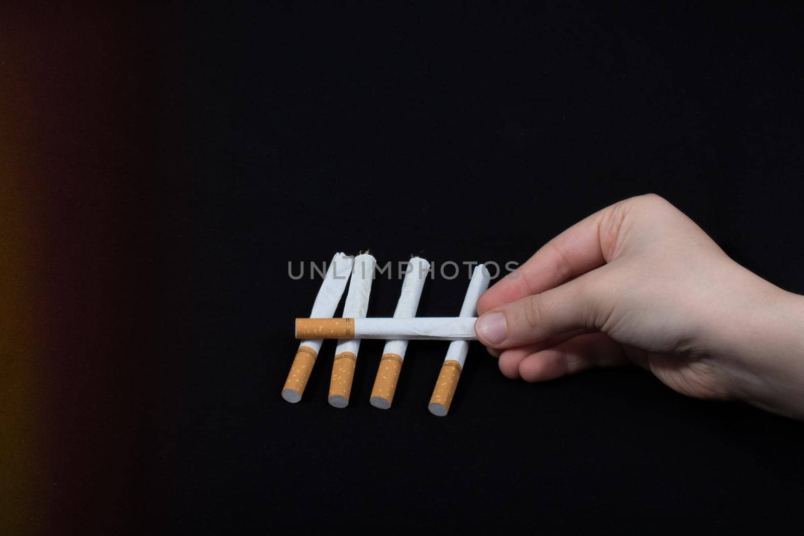 Hand is holding crossed cigarettes on black background