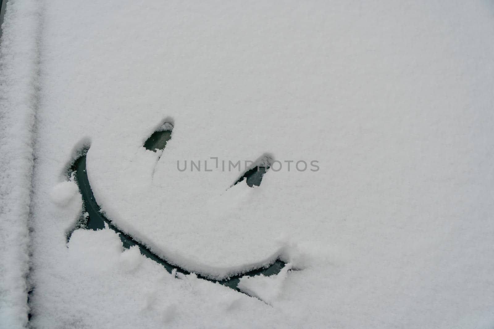 Snow background. Texture of wet snow with a cheerful smiley symbol pattern in the winter window of the car outdoors close-up. Smile in the snow, happy cheerful image. Winter time concept