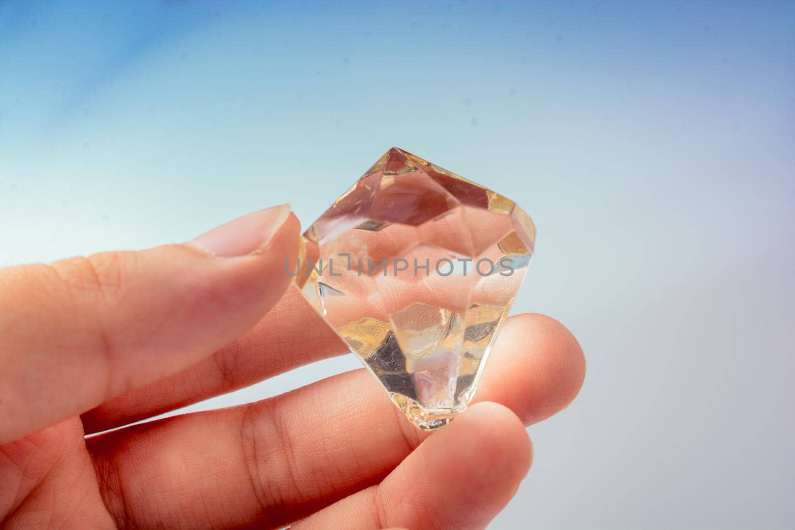 Hand holding a transparent diamond on a white background