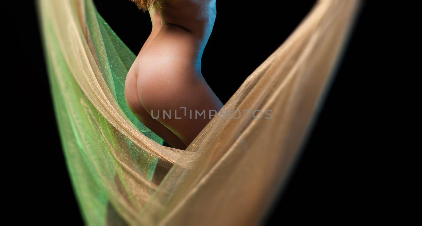 Young nude woman posing in studio with a golden shawl on a dark background. View from the back. 