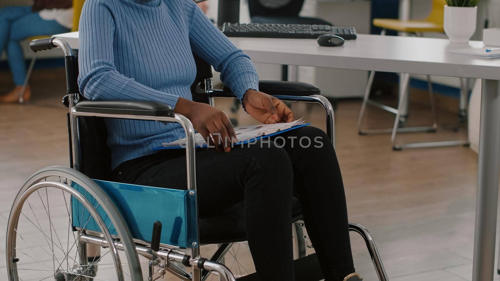 Black woman with disabilities, invalid, disabled paralized handicapped sitting immobilized in wheelchair holding clipboard with financial documents. African manager working in business office room