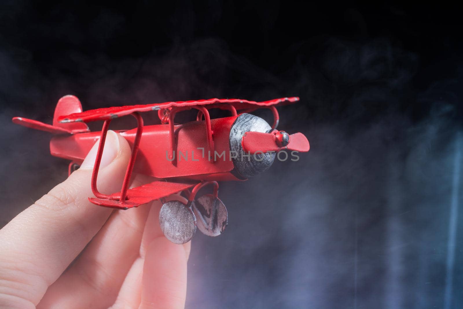 Hand holding a red toy plane on a black background