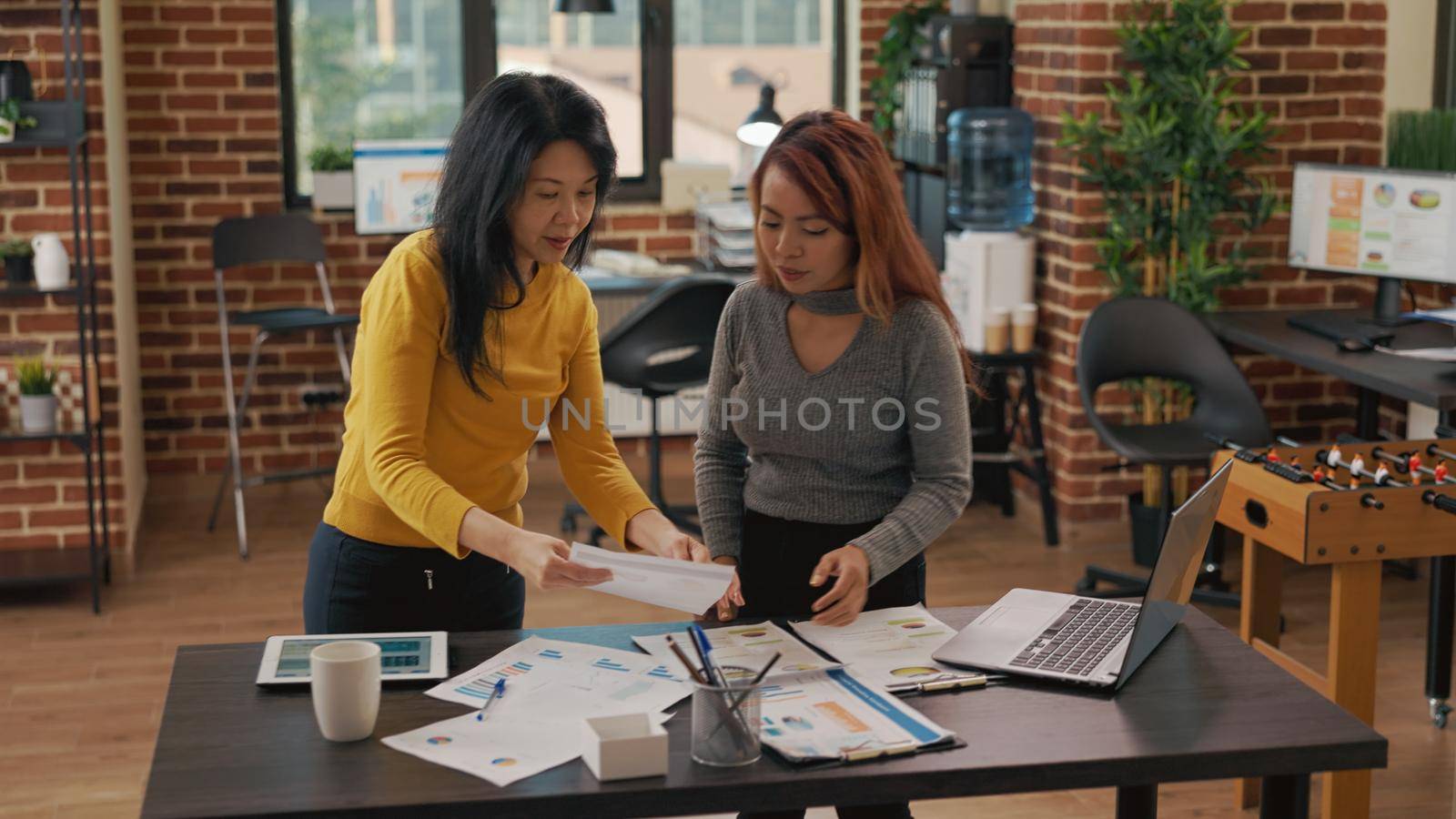 Team of asian women analyzing graphs on paper and tablet to create marketing project, brainstorming strategy ideas for development and business growth. Successful and creative partnership